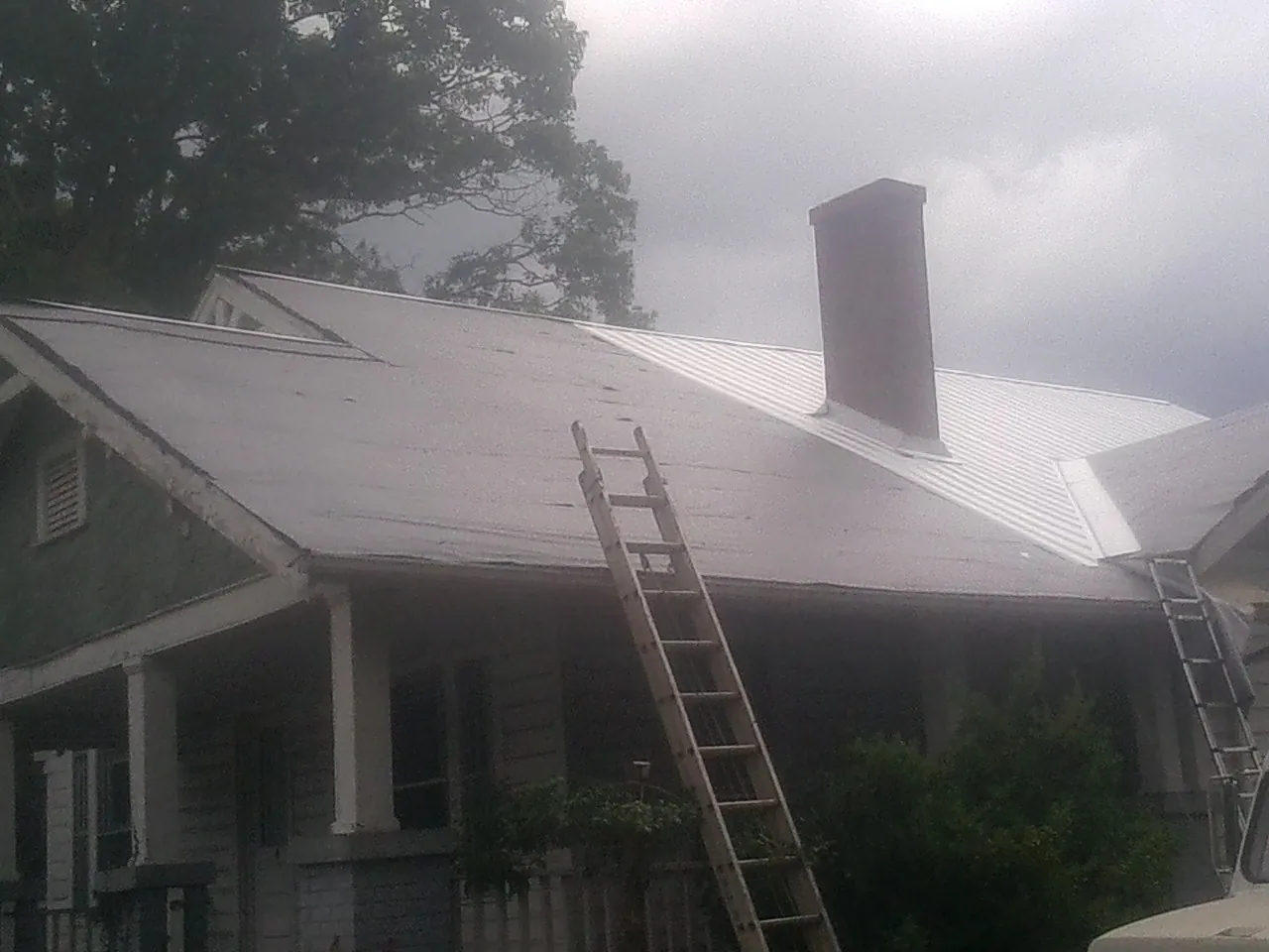 Ladders against a metal roof on an older home with a brick chimney in Mendota