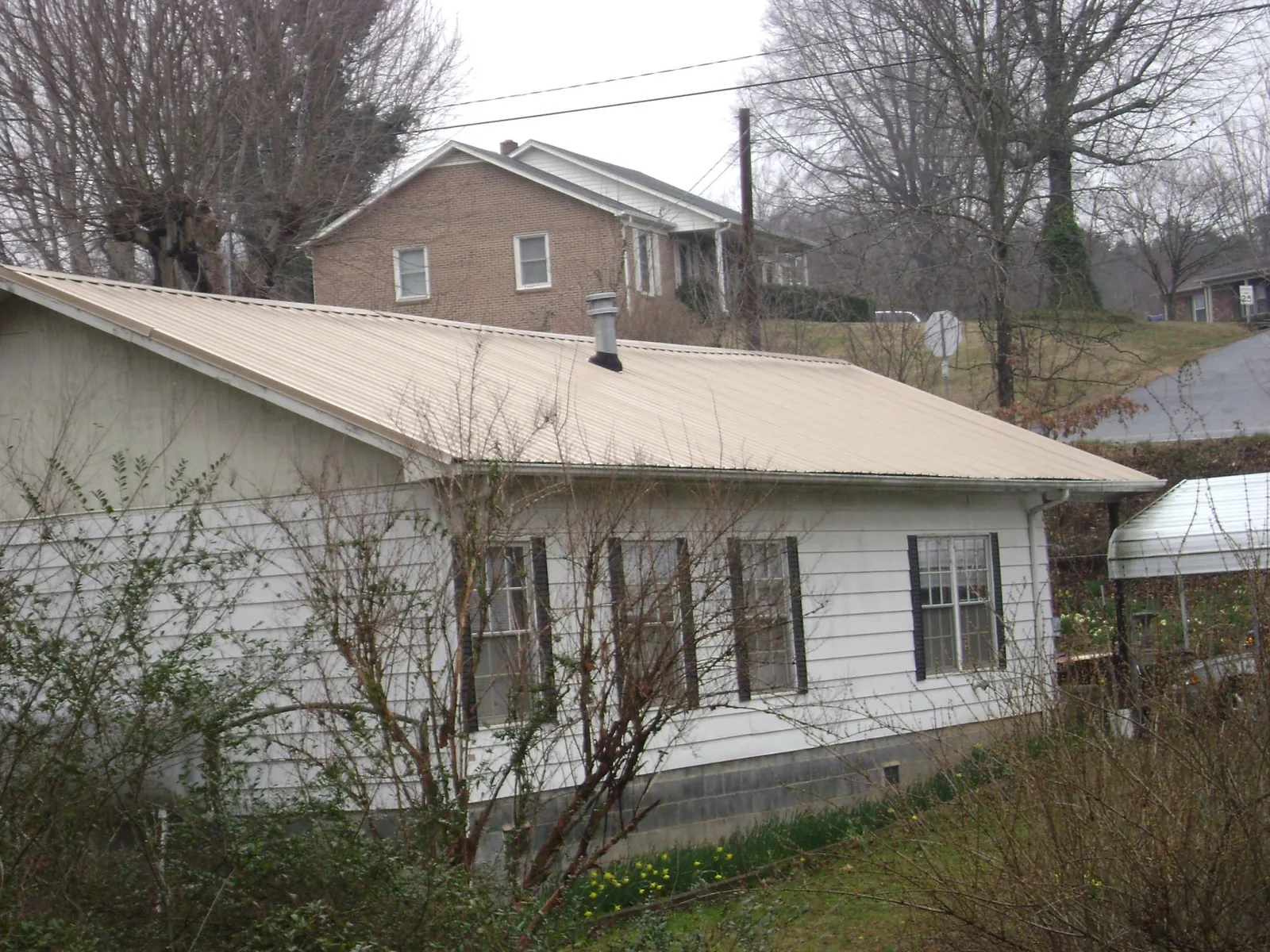 Tan metal roof on a white sided house set into a hillside — Commercial Roofing by Roofing Brothers in Mendota